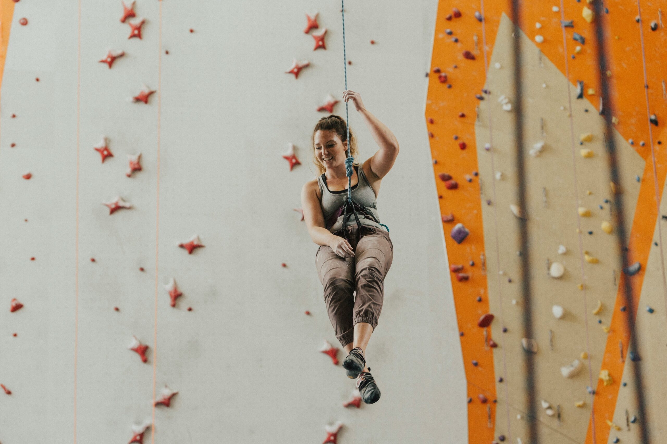 Sarah mid-climb, smiling confidently while wearing a climbing harness.