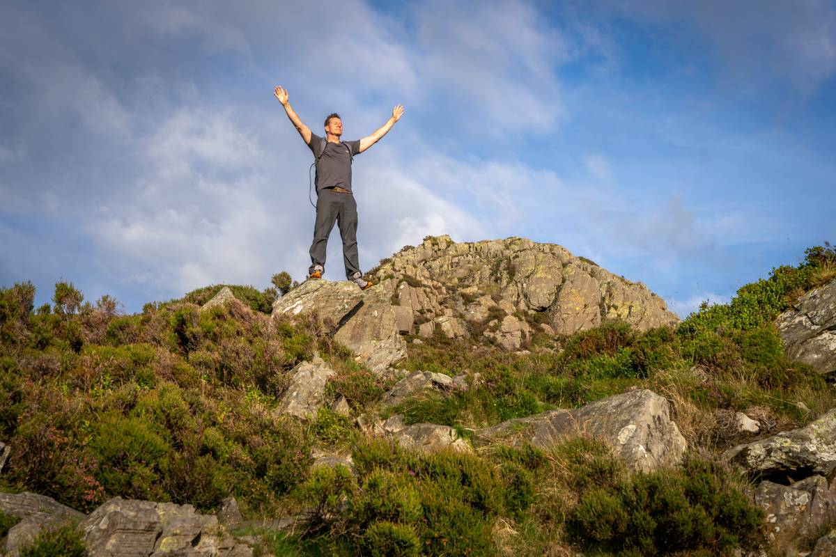 An experienced climber securing a rope outdoors against a scenic mountain backdrop.